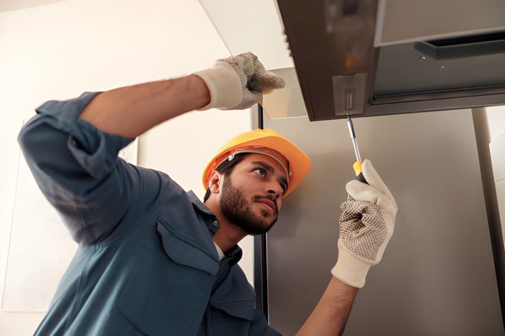 Service man repairing kitchen extractor, replacing filter in cooker hood.