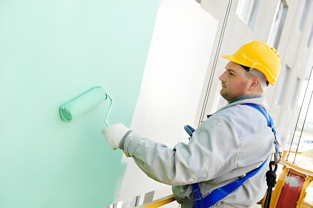 builder worker painting facade of high-rise building with roller
